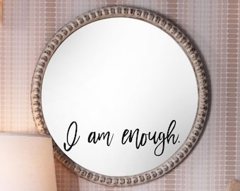 May include: A white round mirror with a decorative beaded frame. The mirror has a black vinyl decal with the text "I am enough."