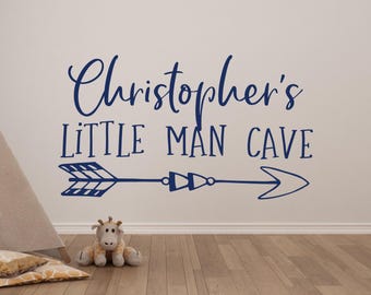 Op de afbeelding: Een blauwe muursticker met de tekst "Christopher's Little Man Cave" en een blauwe pijl met een patroon.