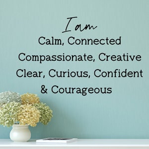 Puede incluir: Una pared azul con el texto "I am Calm, Connected Compassionate, Creative Clear, Curious, Confident & Courageous" escrito en negro. Un jarrón blanco con un ramo de flores blancas y amarillas se encuentra sobre una repisa blanca.