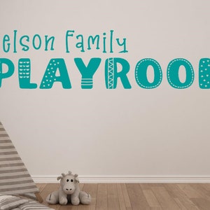 Op de afbeelding: Turquoise blauwe wand sticker met de tekst "Nelson Family Playroom" in een speels lettertype. De sticker heeft decoratieve patronen op elke letter.