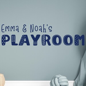 Op de afbeelding: Een blauwe en witte muursticker met de tekst "Emma & Noah's Playroom" in een speels, gepatroneerd lettertype.