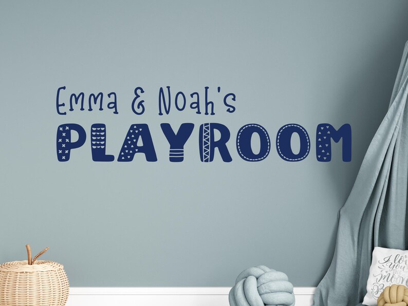 Op de afbeelding: Een blauwe en witte muursticker met de tekst "Emma & Noah's Playroom" in een speels, gepatroneerd lettertype.