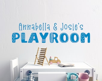Puede incluir: Un letrero de sala de juegos azul y blanco con el texto "Annabella & Josie's Playroom" en una pared blanca. El letrero presenta una fuente lúdica con elementos decorativos.