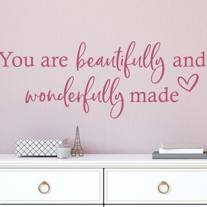 Op de afbeelding: Roze wand sticker met de tekst "You are beautifully and wonderfully made" met een klein hartje aan het einde van de tekst.