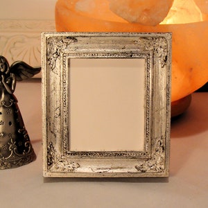 May include: A silver picture frame with an ornate design. The frame is made of metal and has a distressed finish.