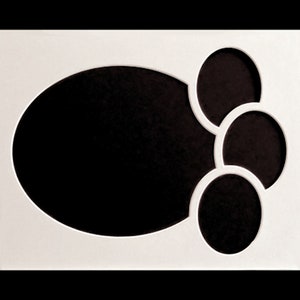 May include: White picture frame with four oval cutouts. The largest cutout is in the center and the three smaller cutouts are clustered together on the right side of the frame.