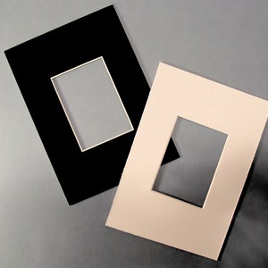 May include: Two mat boards with cut-out openings for framing artwork. One mat board is black and the other is cream.