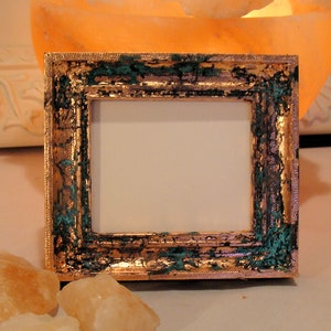 May include: A small, ornate picture frame with a gold and green finish. The frame has a raised, decorative border and a white mat.
