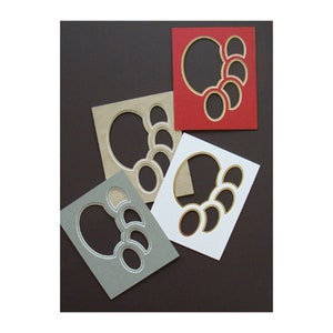 May include: Four square shaped paper frames with a series of oval cutouts. The frames are in red, white, beige, and gray.