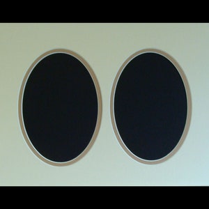 May include: A cream-colored picture frame with two oval openings. The openings have a brown border and a black background.