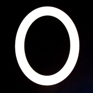 May include: A bright white, illuminated ring against a stark black background. The circular shape is the focal point, creating a bold contrast. The image is simple yet striking, with a clean, modern aesthetic.