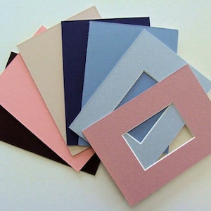 May include: A set of six different colored mat boards, including pink, beige, light blue, dark blue, and two shades of gray. The mat boards are arranged in a fan shape, with the pink mat board on top. The mat boards are all the same size and have a smooth, textured surface.