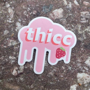 May include: Pink sticker with the word "thicc" in white letters and a red strawberry graphic. The sticker is shaped like a cloud with dripping edges.