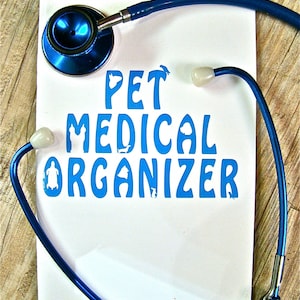 May include: A white card with the text "PET MEDICAL ORGANIZER" in blue lettering. A blue stethoscope with a white earpiece is wrapped around the card.