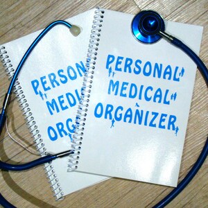 May include: A white spiral bound notebook with the text "PERSONAL MEDICAL ORGANIZER" in blue lettering. A blue stethoscope is wrapped around the notebook.