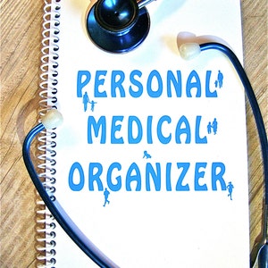 May include: A white spiral bound notebook with the words "PERSONAL MEDICAL ORGANIZER" in blue text. A blue stethoscope is wrapped around the notebook.