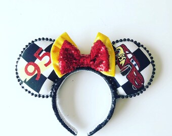 May include: Red and yellow mouse ears with a black and white checkered pattern and a red car with the number 95 on it. The ears have a red bow with yellow accents.