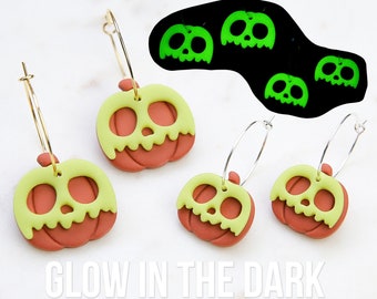 May include: A pair of gold hoop earrings with green and red pumpkin charms. The pumpkins have a skull design and glow in the dark. "Glow in the Dark" is written below the earrings.