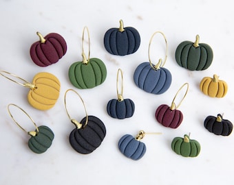 May include: A collection of 14 handmade polymer clay pumpkin earrings in various colors, including green, blue, black, and burgundy. The earrings are all in the shape of a pumpkin and have gold hoops.