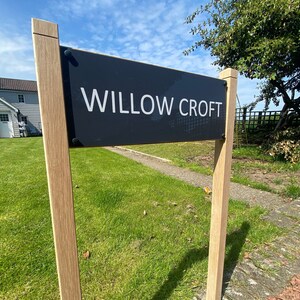 Puede incluir: Un letrero negro con texto blanco que dice "WILLOW CROFT" montado en dos postes de madera. El letrero está frente a un césped verde y una casa.