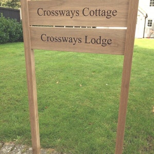 May include: A wooden signpost with two wooden signs. The top sign reads "Crossways Cottage" and the bottom sign reads "Crossways Lodge".