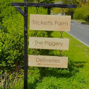 May include: A wooden sign with three lines of text. The top line reads "Tricketts Farm", the middle line reads "The Piggery", and the bottom line reads "Deliveries" with an arrow pointing to the right.