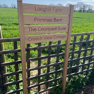 May include: A wooden sign with the text "Longhil Farm", "Primrose Barn", "The Courtyard Suite", and "Creech View Cottage" on it. The sign is attached to a wooden fence.