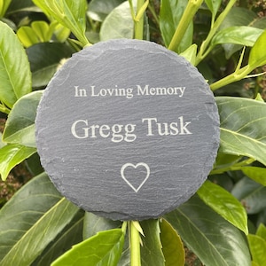 Peut inclure: Une plaque commémorative ronde en ardoise gris foncé avec l'inscription "In Loving Memory Gregg Tusk" et un symbole de cœur. La plaque est entourée de feuilles vertes.