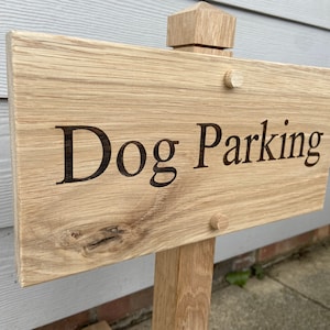 Könnte beinhalten: Ein Holzschild mit dem Text "Dog Parking", der in die Oberfläche gebrannt ist. Das Schild ist an einem Holzpfosten befestigt.