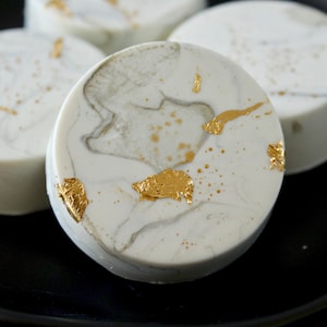 May include: Three round white cakes with gold leaf accents on a black plate. The cakes have a marbled appearance.