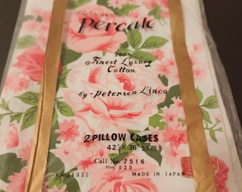 May include: A package of two pillow cases featuring a pink floral pattern on a white background. The packaging text reads Percale, 100% Finest Luxury Cotton by Petersen Linco, 2 Pillow Cases 42 inches by 36 inches, Call No. 7516, Pink #20, RN 14312, Made in Japan.