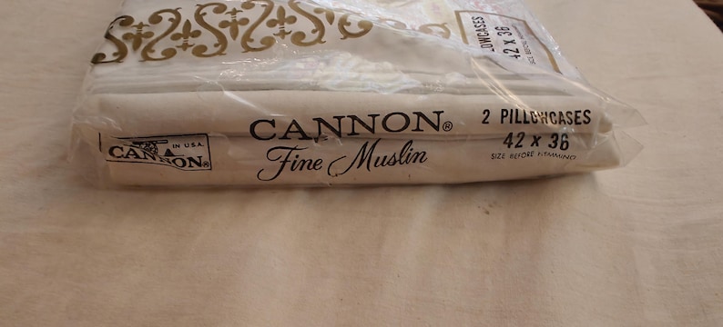 Może przedstawiać: Opakowanie dw&oacute;ch poszewek na poduszki Cannon Fine Muslin. Poszewki są białe, a opakowanie jest z przezroczystego plastiku. Tekst na opakowaniu brzmi "2 Poszewki na poduszki 106.68 x 91.44 cm".