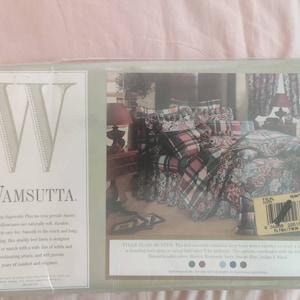 May include: A Wamsutta Supercale Plus bed linen package featuring a twin size set with a plaid and floral pattern in shades of hunter green, burgundy, and navy blue. The packaging includes product text, a barcode, and a room setting illustration.