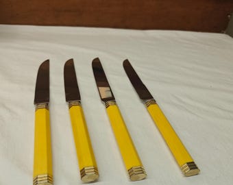 May include: Four dinner knives with polished silver-tone metal blades and bright yellow handles. Each handle features a hexagonal shape with subtle vertical ridges and gold-tone metal accents at the top and bottom ends of the grip.