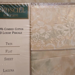 May include: A package of Orosciel Home Fashions twin flat sheet in Laguna. The packaging features the text 100% Combed Cotton 200 Luxury Percale. The sheet is a light cream color with a subtle, tonal floral pattern visible through the clear plastic.
