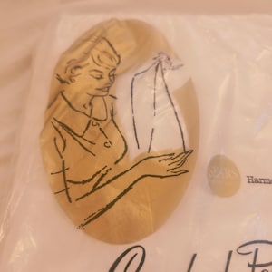 May include: A white plastic packaging bag featuring a gold oval graphic with a black line drawing of a person holding a garment. The text Sears and Harmony are visible on the surface, along with partial cursive lettering at the bottom edge.