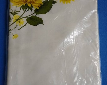 May include: A white rectangular cloth packaged in clear plastic, featuring a printed design of yellow chrysanthemums with green leaves in the upper corner. A blue label at the bottom reads Sun Glo Hand Printed Cloth Drip Dry Printorama.