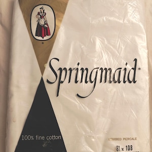 May include: A white Springmaid bed sheet packaged in clear plastic. The label features a gold triangular graphic with a woman in a red dress, the text 100% fine cotton, Combed Percale, and 81 x 108 Double Bed Size. The packaging is sealed and rectangular.