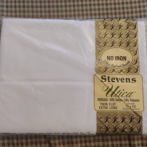 May include: A packaged white twin flat extra long percale sheet. The packaging includes a label with the text "NO IRON" and the brand name "Stevens Utica". The sheet is 72 x 115 inches before hemming.