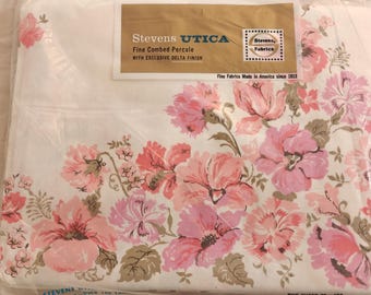 May include: A white bed sheet in plastic packaging featuring a pink and coral floral pattern. The label reads Stevens UTICA Fine Combed Percale with Exclusive Delta Finish, and the bottom text indicates one sheet 72 x 109 inches.