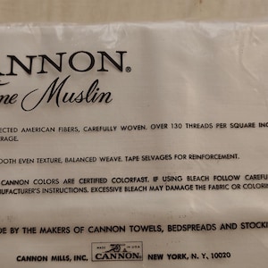 Może przedstawiać: Opakowanie tkaniny Cannon Fine Muslin. Biała tkanina znajduje się w przezroczystym plastikowym opakowaniu. Tekst na opakowaniu brzmi "CANNON. Fine Muslin" i zawiera szczeg&oacute;ły dotyczące składu i instrukcji pielęgnacji tkaniny.