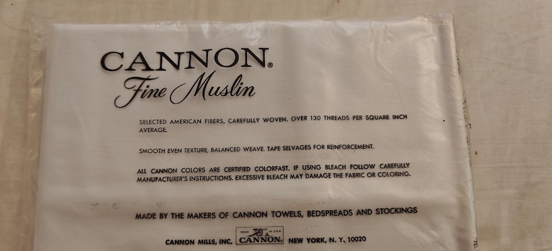 Może przedstawiać: Opakowanie tkaniny Cannon Fine Muslin. Biała tkanina znajduje się w przezroczystym plastikowym opakowaniu. Tekst na opakowaniu brzmi "CANNON. Fine Muslin" i zawiera szczeg&oacute;ły dotyczące składu i instrukcji pielęgnacji tkaniny.