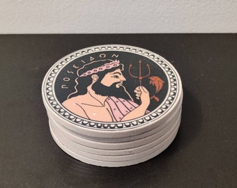 May include: A stack of circular ceramic coasters featuring a graphic illustration of the Greek god Poseidon. The design includes a black background, a pink-toned figure with a beard and crown, a trident, a small fish, and the text POSEIDON.