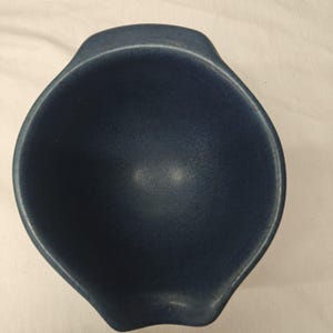 May include: A deep, round ceramic bowl in a solid matte navy blue finish. The bowl features a smooth, speckled texture throughout its surface and includes two integrated, slightly raised handles on opposite sides for a secure grip.