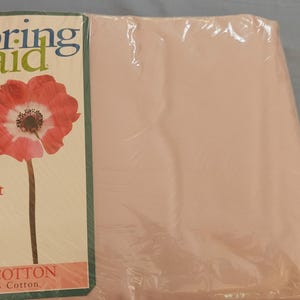 May include: A package of a full flat sheet from Springmaid, made of 100% cotton. The packaging features a red and white flower illustration. The sheet is a solid light pink color and has a 200 thread count.