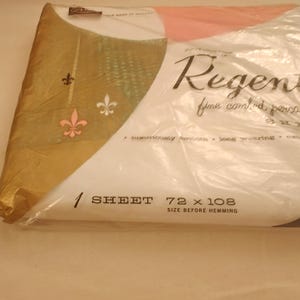 May include: A white sheet in plastic packaging labeled Regent fine combed percale. The packaging features a gold corner with three fleur-de-lis icons in black, white, and pink. Text indicates 1 SHEET 72 x 108 SIZE BEFORE HEMMING.