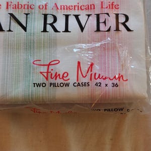 May include: A package of two "Fine Muslin" pillowcases, 42 x 36 inches, with the text "AN RIVER" and "Fabric of American Life". The packaging has a red, green, and brown design.