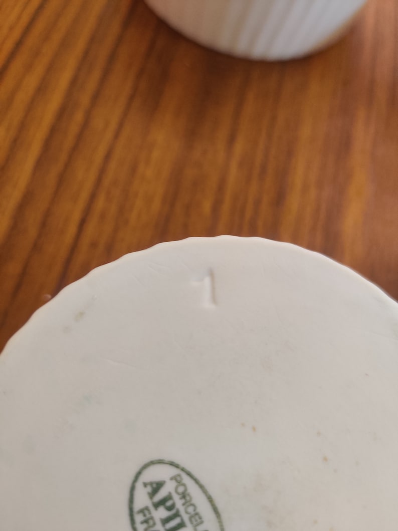 May include: Close-up of a white porcelain object with a ribbed design and the number "1" stamped on the bottom. The object has a small green and white label with text. The background is a wooden surface.