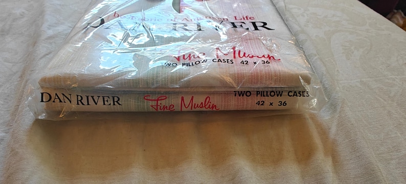 May include: A package of Dan River Fine Muslin pillowcases. The package is clear plastic, and the pillowcases are folded inside. The text "TWO PILLOW CASES 42 x 36" is printed on the package. The pillowcases measure 42 inches by 36 inches.