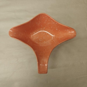 May include: A salmon-colored bowl with a unique four-pointed, asymmetrical shape and a speckled white pattern throughout the surface. The bowl features a wide, open basin that tapers into a single elongated handle-like extension at the base.
